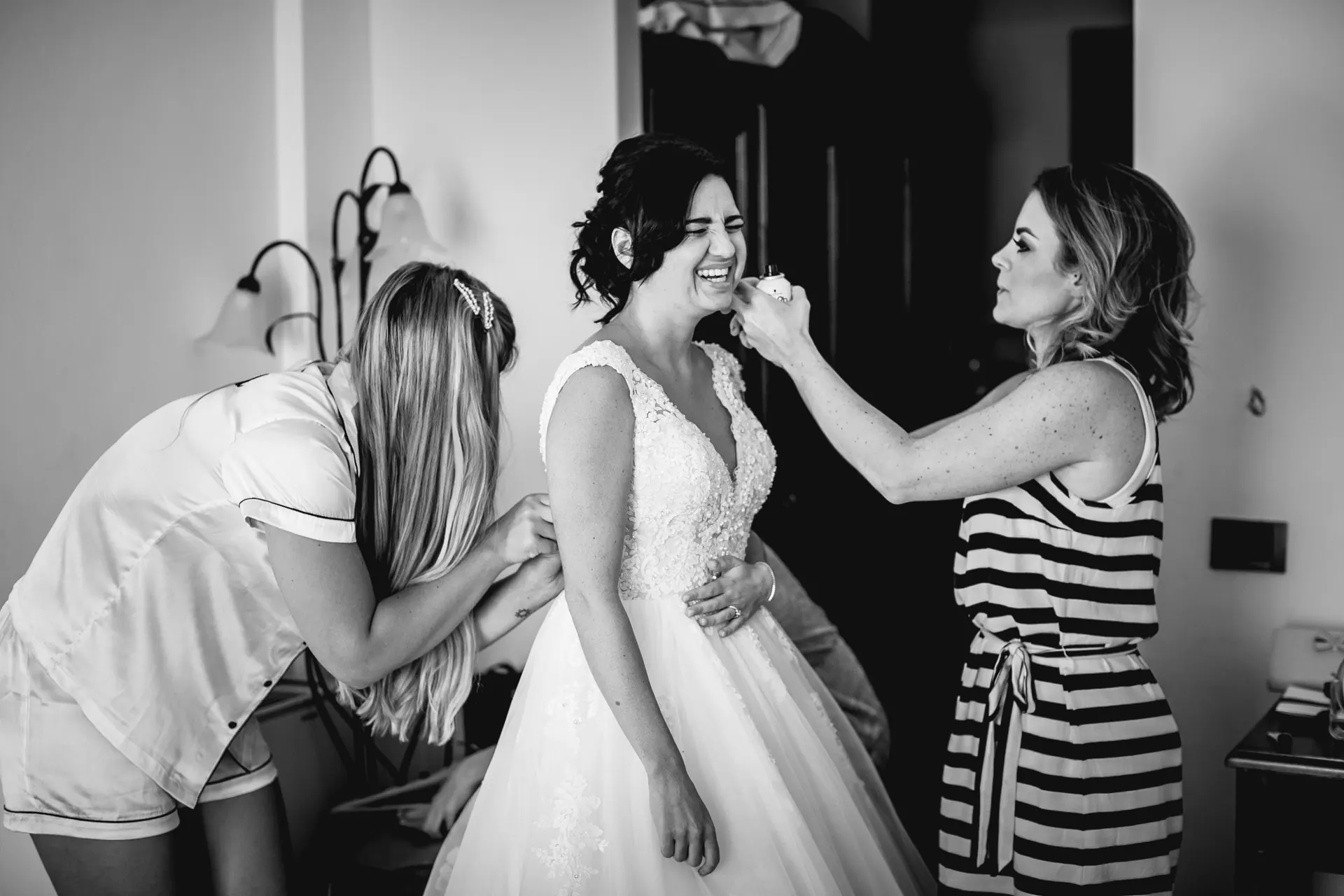 Laughing bride in her wedding dress having her makeup touched up — bridal hair and makeup by Jade Victoria, Surrey